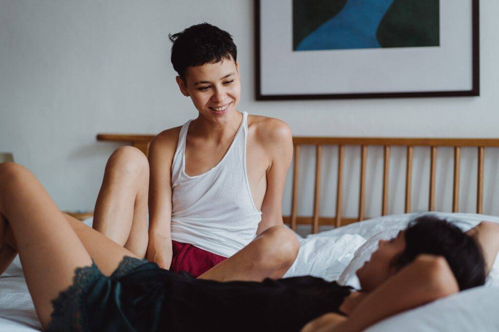 Two women are sitting on a bed and having a conversation while smiling at eachother